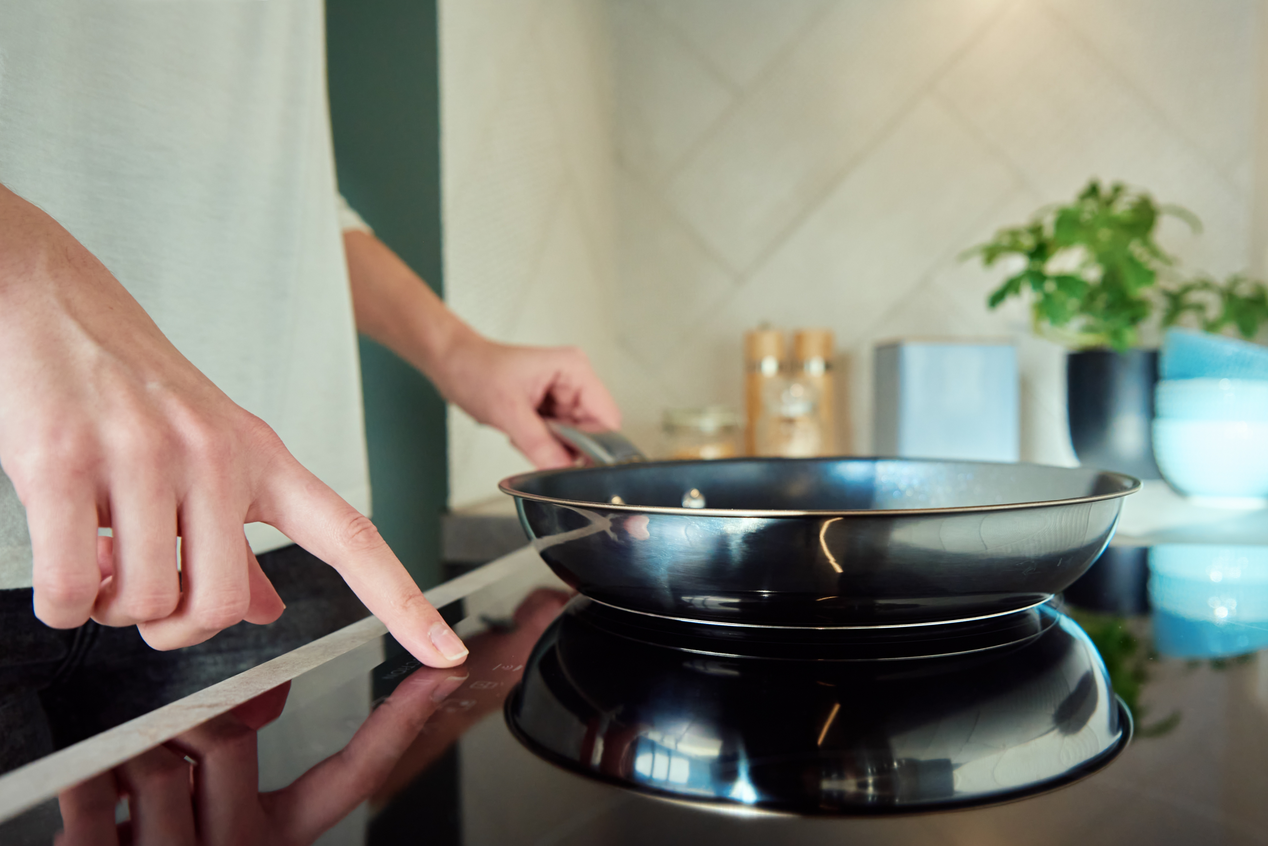 Close-up of someone using a sleek black induction cooktop with touch controls.