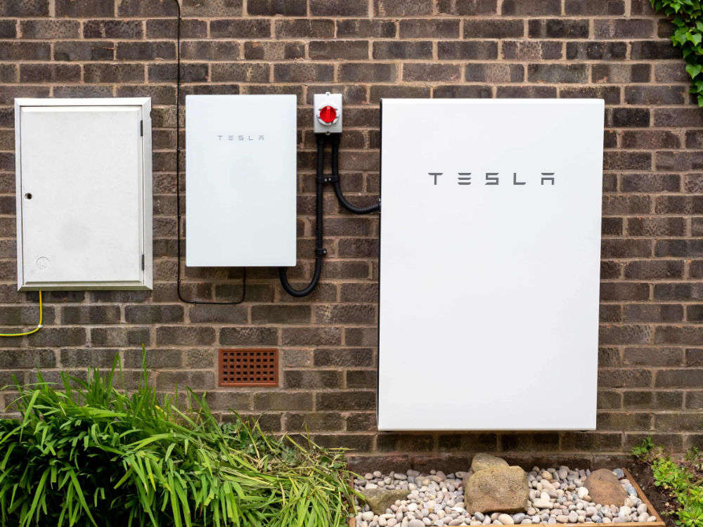 Tesla Powerwall battery installed on the exterior brick wall of a home.
